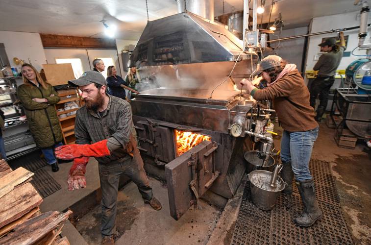 Dan Waters feeds the evaporator as Jasmine Atsalis-Gogel checks on the maple syrup during a tour by state and local officials at the Blue Heron Farm sugarhouse in Charlemont on Monday.