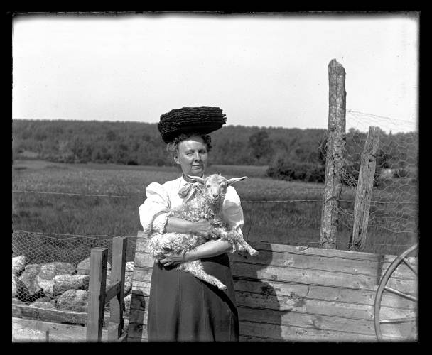 A woman and her lamb or young sheep. Her hat seems precariously balanced.