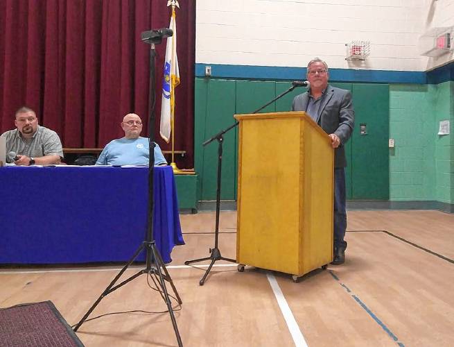 Moderator Richard Peabody stands behind the podium during Erving’s Annual Town Meeting at Erving Elementary School on Wednesday as Selectboard Chair Jacob Smith, left, and Selectboard member James Loynd, middle, look on.