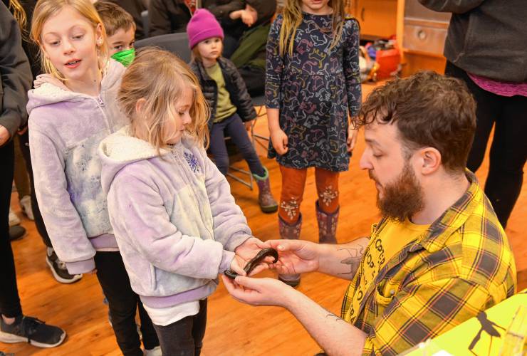 Iris Fisher, 8, and her sister Ivie Fisher, 5, of Petersham, take turns holding an African giant millipede after a presentation by Bryan Man, also known as Professor Bugman, at the Athol Public Library in February.