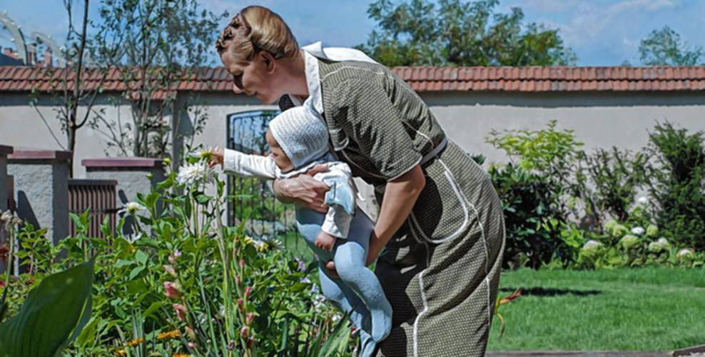 Sandra Hüller, playing Hedwig Höss, gives her newborn daughter a close look at the family garden outside Auschwitz concentration camp in a scene from “The Zone of Interest.”