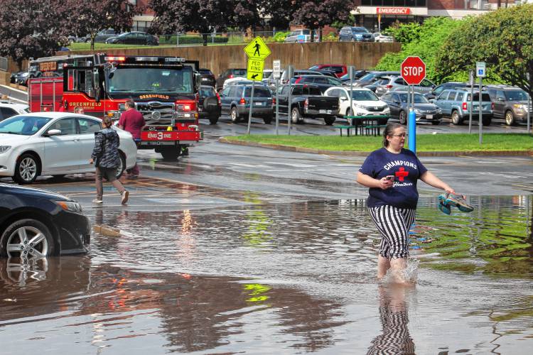 Samantha Booker, who works at Greenfield Family Medicine, walks through a flooded portion of the parking lot in Greenfield in July.