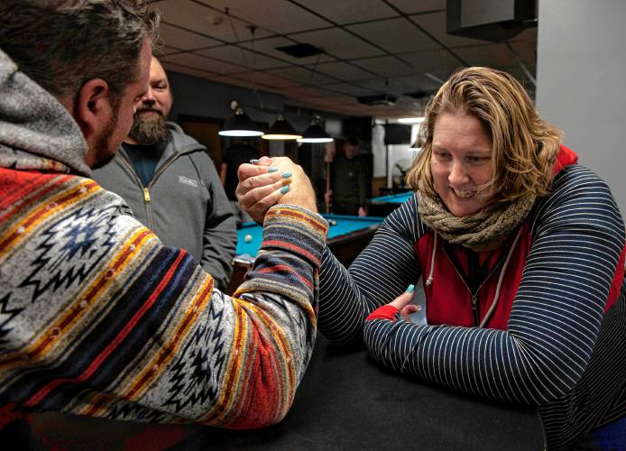 Rose Lynch demonstrates a practice session with Donald Carberry, a co-sponsor for the arm wrestling event The Pulaski Pull Down, while Chris Parker watches at Se7ens Sports Bar and Grill in Easthampton Thursday evening, Dec. 6, 2023.