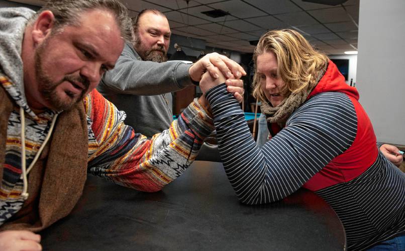 Donald Carberry, a co-sponsor for the arm wrestling event The Pulaski Pull Down, and Rose Lynch demonstrate a practice session while Chris Parker, middle, sets them up, at Se7ens Sports Bar and Grill in Easthampton on Dec. 6.