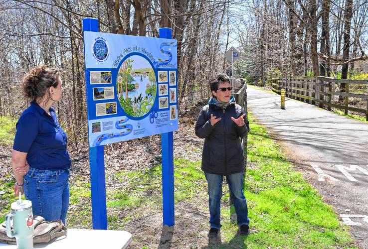 In celebration of Earth Day on Monday, Montague Clean Water Facility Superintendent Chelsey Little and Greenfield artist Mary Chicoine, right, reveal a new informational sign marking the entrance to the bike path on Greenfield Road in Montague. Although Lahri Bond was chosen during a call for artists to design a mural on the side of the wastewater treatment plant a few years ago, Chicoine’s work also stood out. So, Little spearheaded a project to use Chicoine’s artwork on an informational sign about how the wastewater plant functions and the local flora and fauna. With approval from the state Department of Conservation and Recreation and the town of Montague, the new sign was assembled by Hale Custom Signs and revealed on Monday afternoon.