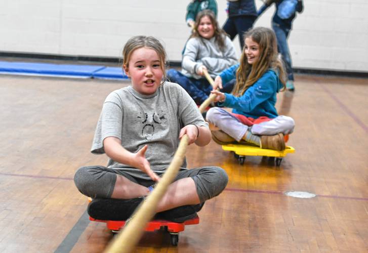 Fourth grade students at Conway Grammar School pull themselves along on scooters in the gymnasium on Tuesday in celebration of Read Across America Day. In front is Louise Brownlow, followed by Olivia Craig and Serena Streeter.