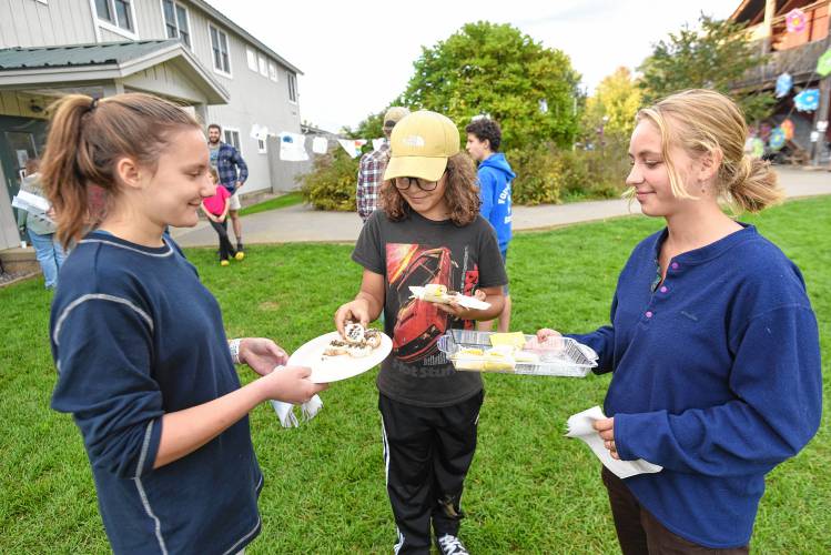 Freshman Olivia Long, left, and Penelope Peters, right, offer hors d’oeuvres to seventh grader Aksel Kotright-Clark, center, at the Hispanic Heritage Month celebration at Four Rivers Charter Public School on Friday evening.