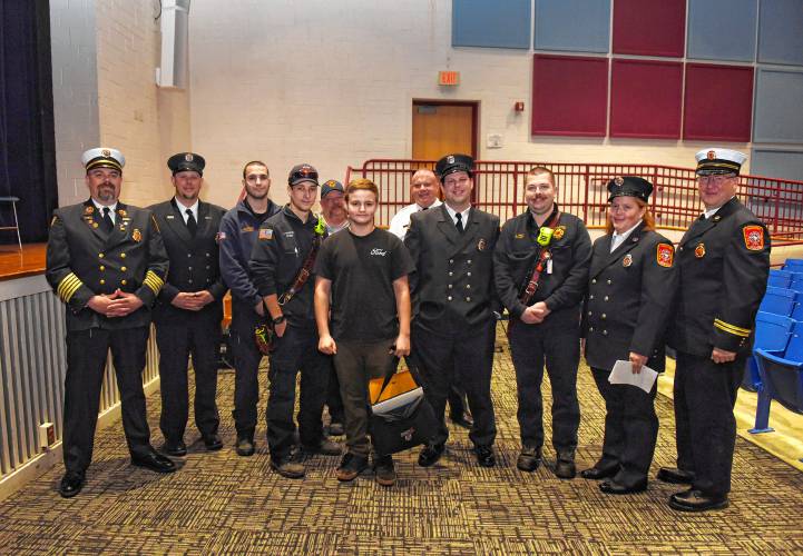 Ralph C. Mahar Regional School student Joel Wilkey, center, stands with local and state fire personnel after an assembly in his honor at the school Friday morning.