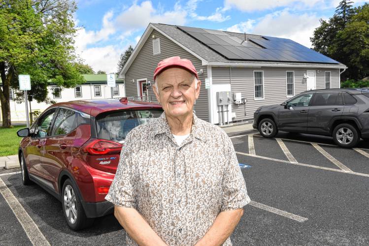 Greenfield resident William “Bill” Ashley stands in front of his electric vehicle and the donated solar panels on the Greenfield Department of Public Works administrative office building on Wells Street.
