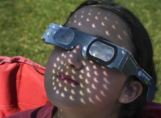 Hazel Singh, 11, of Northfield, has images of the eclipse projected on her face from a kitchen colander held between her face and the sun at an eclipse viewing event held at Pioneer Valley Regional School on Monday.
