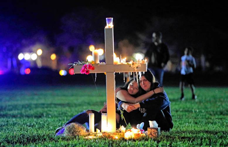 People comfort each other as they mourn at one of 17 crosses after a candlelight vigil on Feb. 15, 2018, for the victims of the shooting at Marjory Stoneman Douglas High School, in Parkland, Fla.