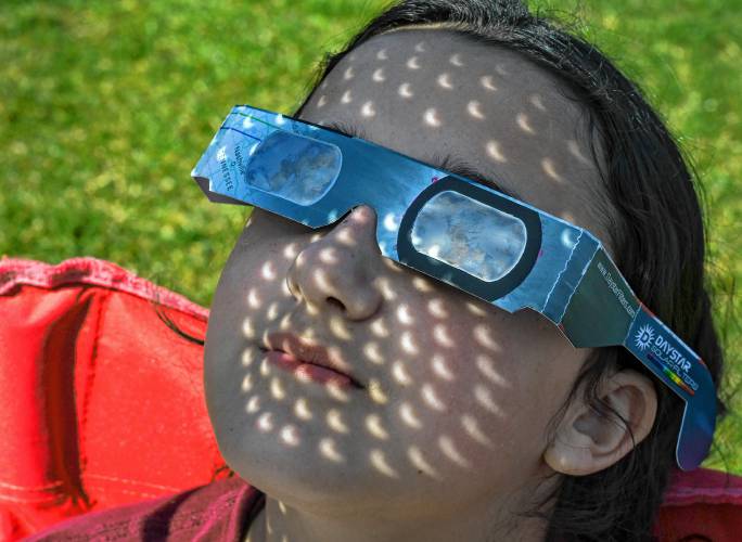 Hazel Singh, 11, of Northfield, has images of the eclipse projected on her face from a kitchen colander held between her face and the sun at an eclipse-viewing event held at Pioneer Valley Regional School on Monday.