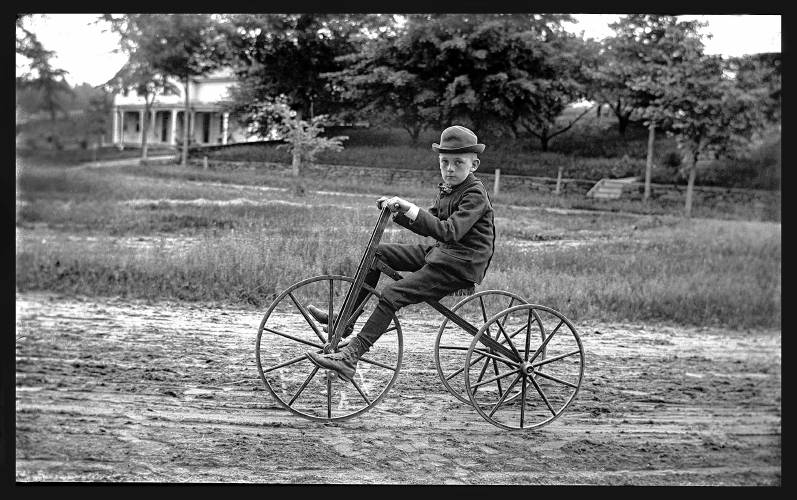 An unknown young boy rides a 19th century/early 20th century tricycle. 