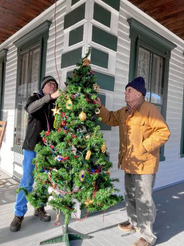 Orange Historical Society members Terry Reed (left) and Frank Schiappa secure a Christmas tree on the porch of the 41 North Main St. museum after having strung colored lights along the porch railing. Not pictured, Society President Kathryn Schiappa and board of directors member Ann Reed deck the environs with fresh winter greenery and holly.