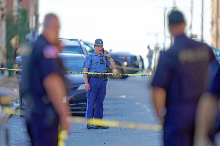 Members of law enforcement stand near police tape while investigating the scene where multiple people were shot in Holyoke in October 2023.