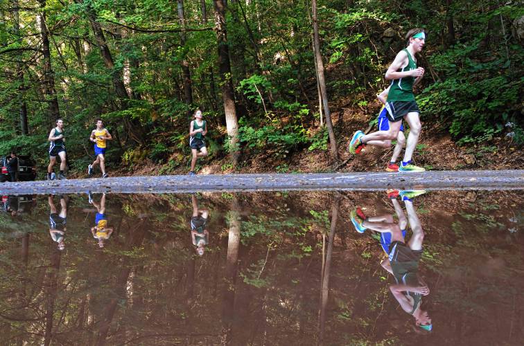 Reflected through a puddle, runners move through the course at Highland Park on Tuesday afternoon.